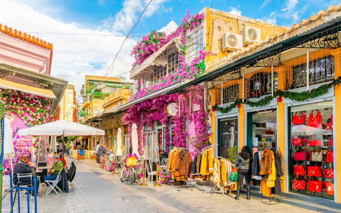 Shops and cafes in a vibrant street near Plaka, Athens, Greece, with colorful flowers and clothing displays.