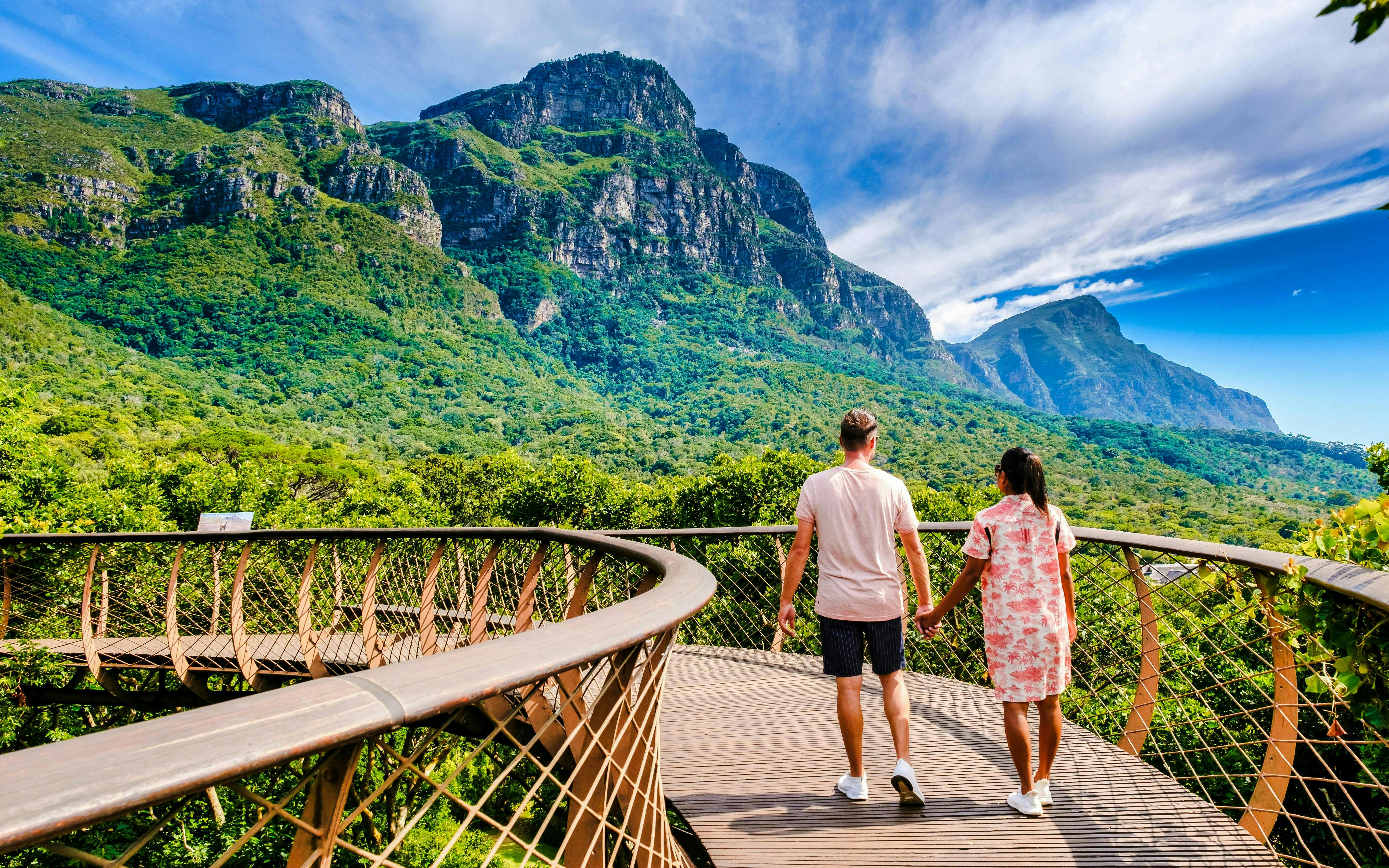 Couple walking on canopy bridge at Kirstenbosch Gardens with mountain view.