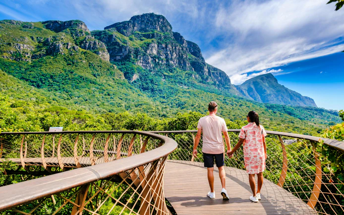 Couple walking on canopy bridge at Kirstenbosch Gardens with mountain view.