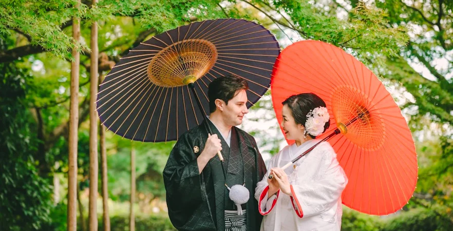 Couple in traditional attire with umbrellas during a tea ceremony experience in a Japanese garden.