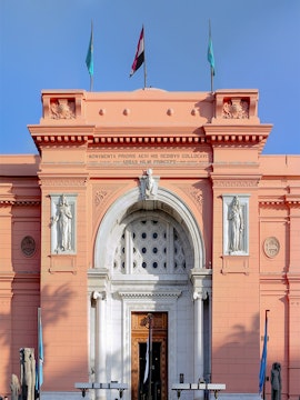 Facade of the Egyptian Museum in Cairo with flags and statues.