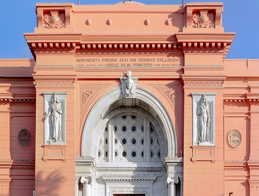 Facade of the Egyptian Museum in Cairo with flags and statues.