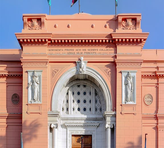Facade of the Egyptian Museum in Cairo with flags and statues.