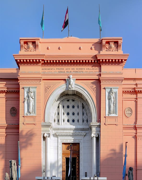 Facade of the Egyptian Museum in Cairo with flags and statues.