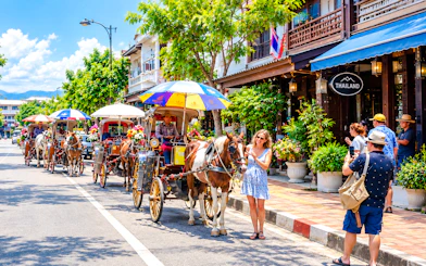 Horse-drawn carriages on a street in Chiang Mai, Thailand, with tourists taking photos.