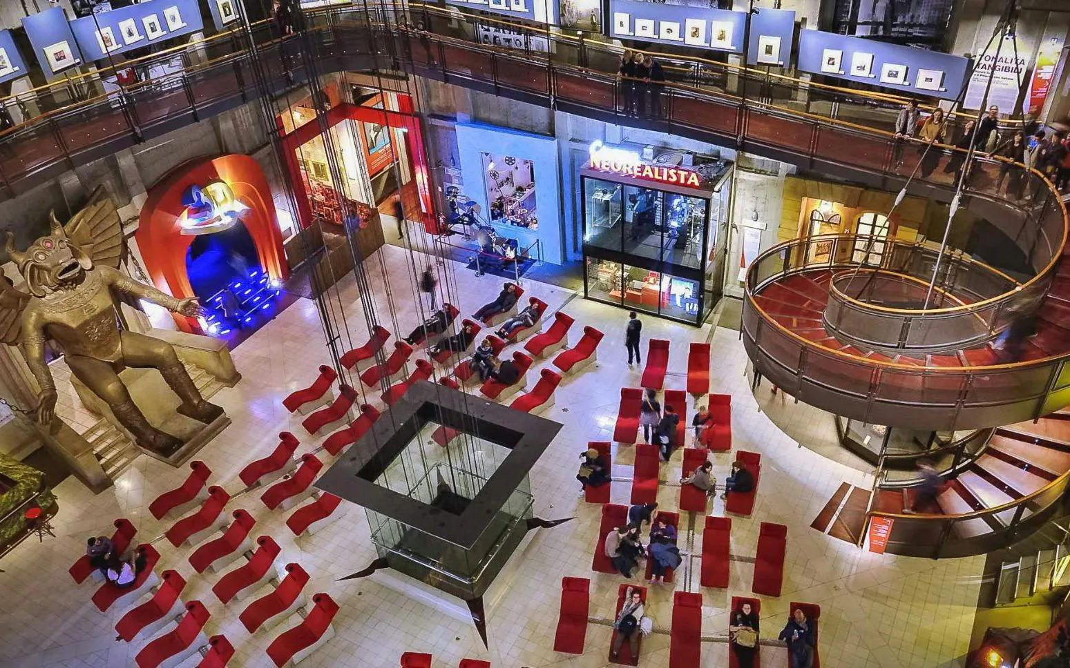 Visitors in the atrium of the National Museum of Cinema, Turin, with red seating and a large statue.