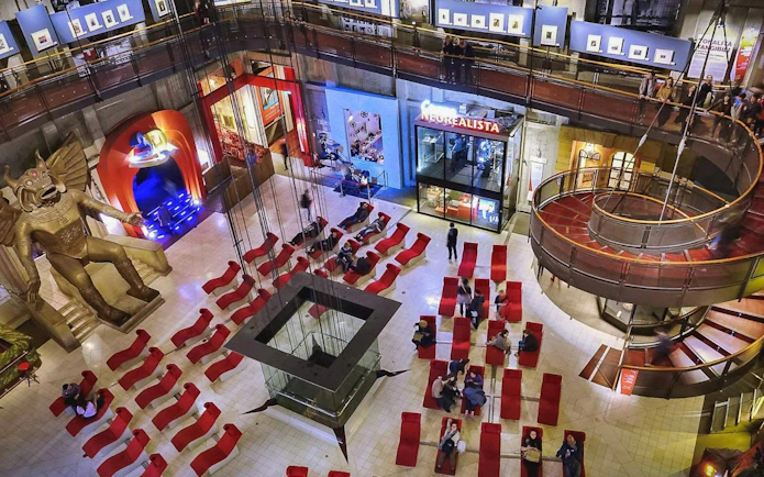 Visitors in the atrium of the National Museum of Cinema, Turin, with red seating and a large statue.