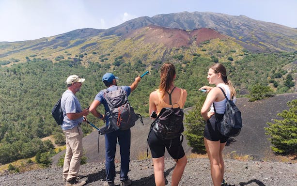 Group hiking on Mount Etna with guide pointing at volcanic landscape.