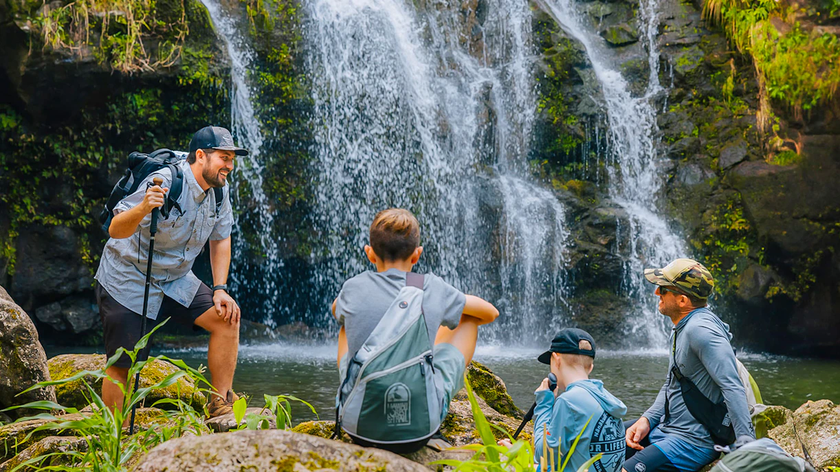 Guests hiking near Kohala Waterfalls in lush greenery.