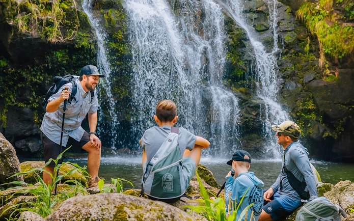 Guests hiking near Kohala Waterfalls in lush greenery.