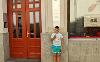 Child standing outside a historic building in Prague, part of the Alchemy Mission city exploration game.