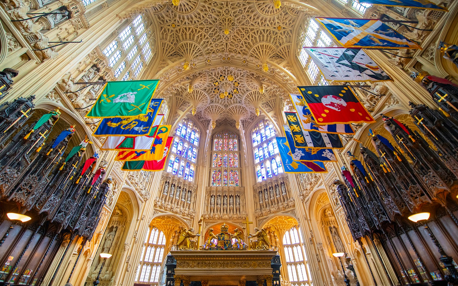 Henry VII Lady Chapel interior with ornate ceiling and colorful heraldic banners.