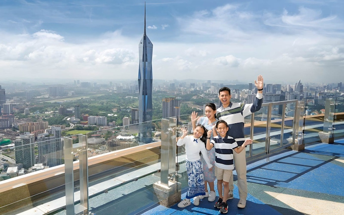 Family enjoying view from KL Tower Sky Deck, Kuala Lumpur skyline in background.