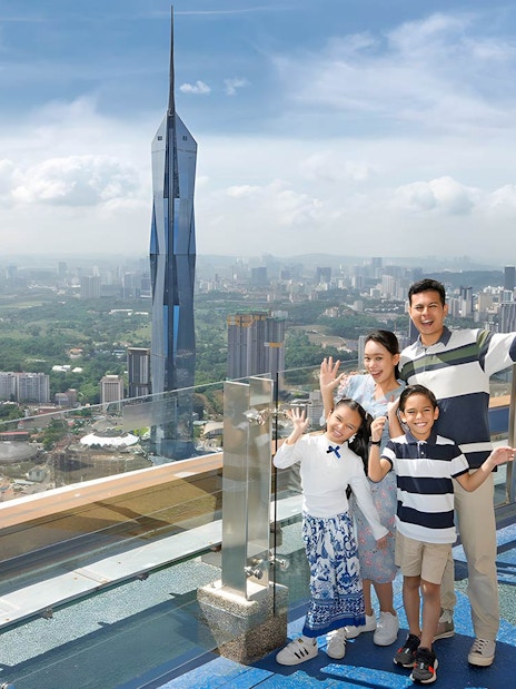 Family enjoying view from KL Tower Sky Deck, Kuala Lumpur skyline in background.