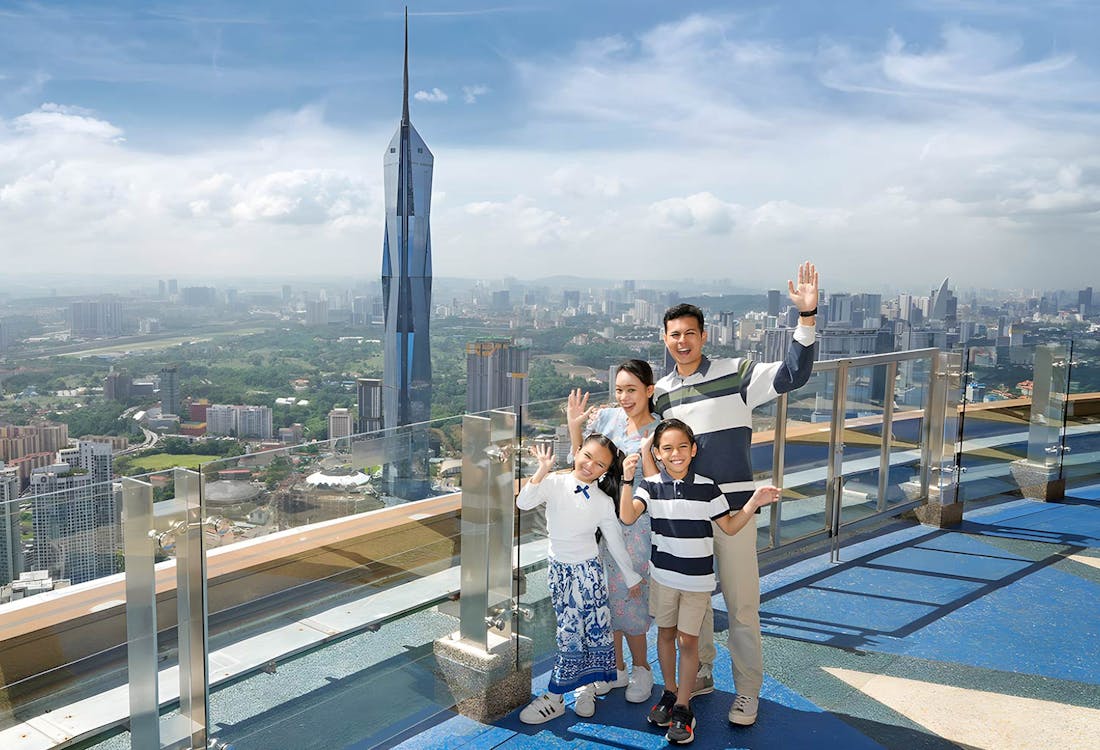 Family waves from KL Tower sky deck, Kuala Lumpur. City skyline view.