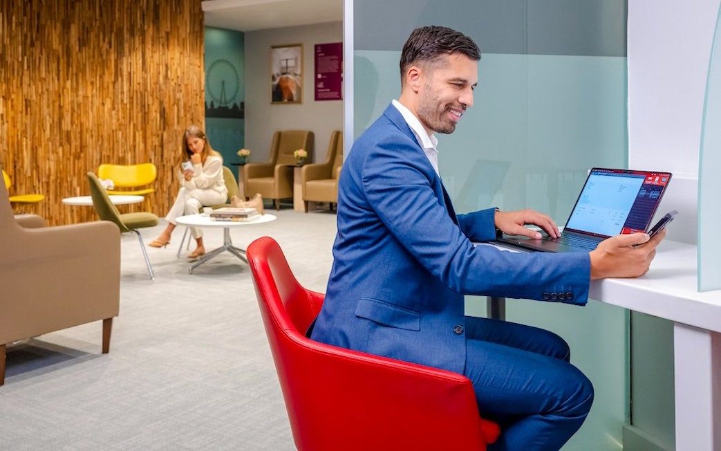 Man working on laptop in Plaza Premium Lounge, London, with seating area in background.