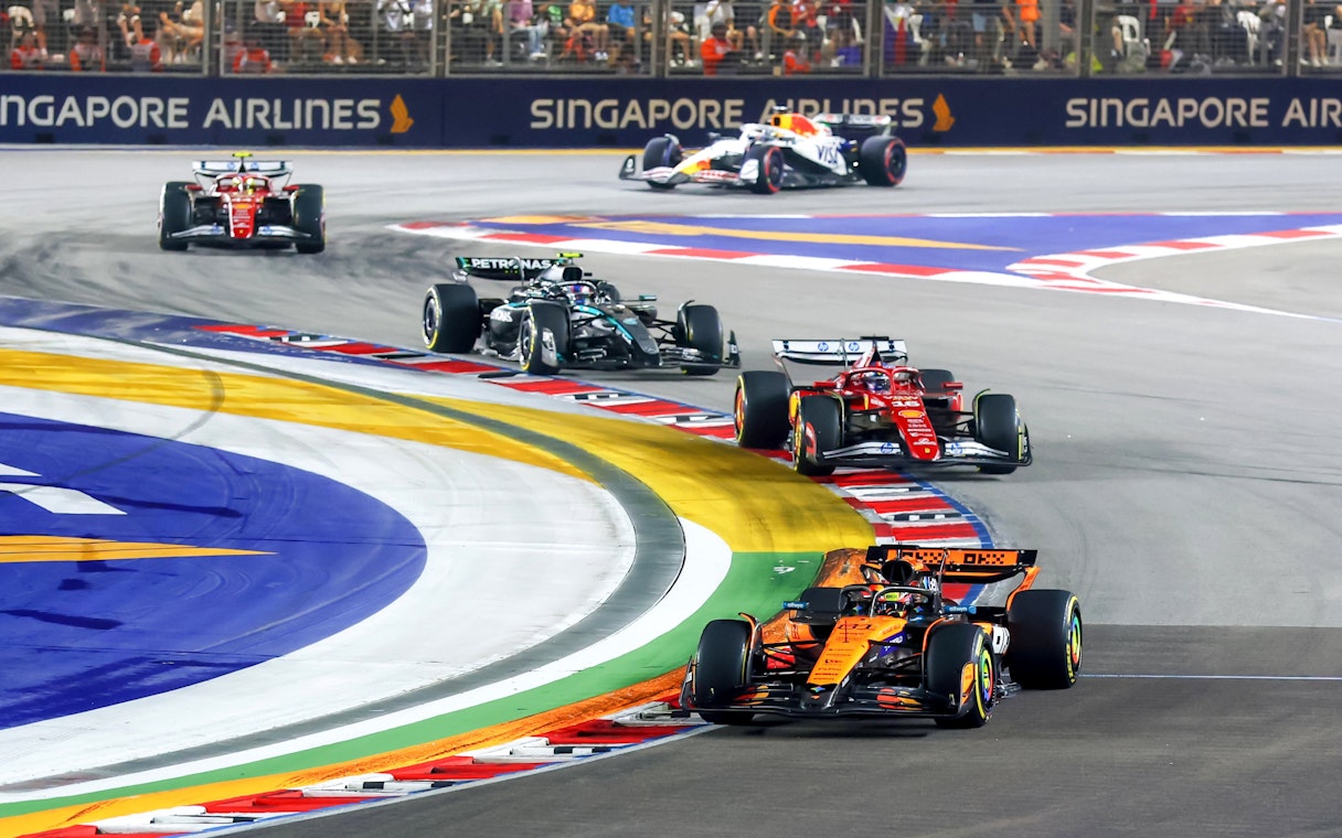Race cars navigating a sharp turn on the Singapore Grand Prix track.