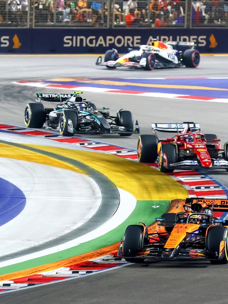 Race cars navigating a sharp turn on the Singapore Grand Prix track.