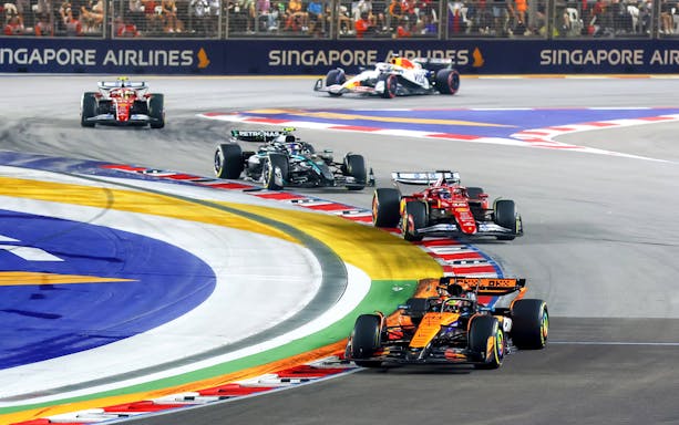 Race cars navigating a sharp turn on the Singapore Grand Prix track.