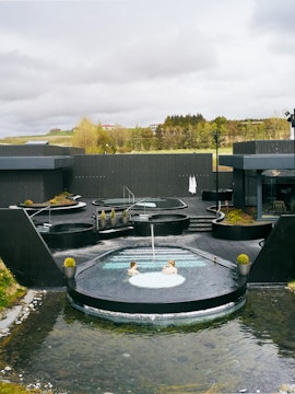 Krauma Geothermal Baths outdoor pools with visitors relaxing in Icelandic landscape.