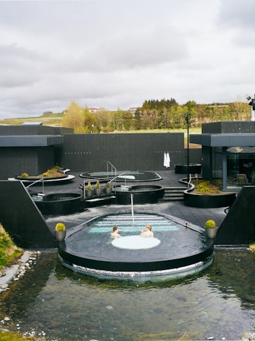 Krauma Geothermal Baths outdoor pools with visitors relaxing in Icelandic landscape.