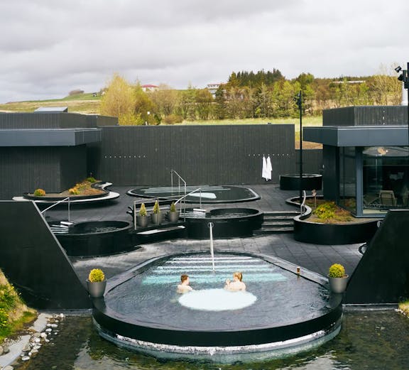 Krauma Geothermal Baths outdoor pools with visitors relaxing in Icelandic landscape.