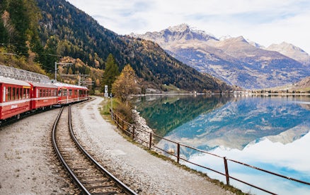 Red Bernina train traveling along a lake with mountain reflections near St. Moritz.