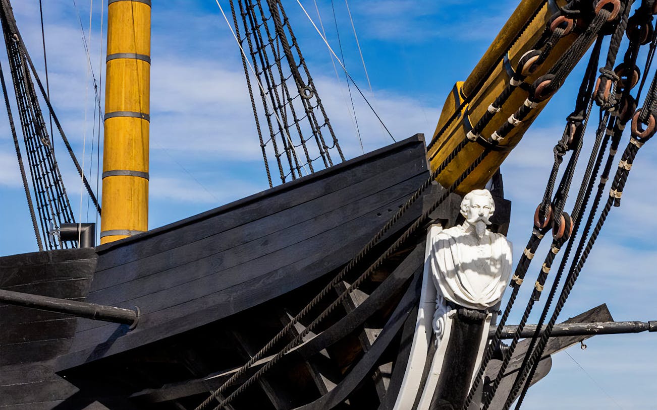 Frigate D. Fernando II e Glória bow with figurehead and rigging against blue sky.