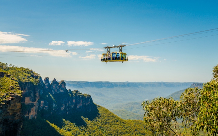 Cable car over Blue Mountains with scenic view of cliffs and forest.