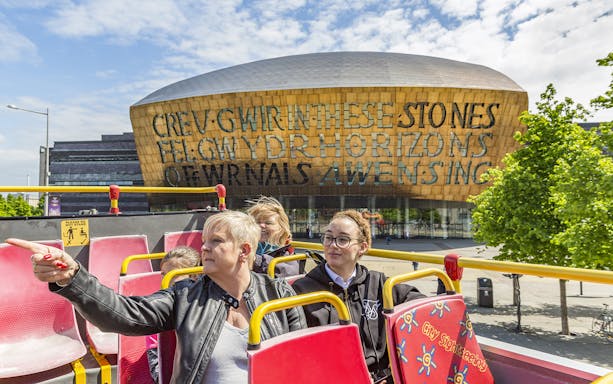 Cardiff hop-on hop-off bus tour with passengers near Wales Millennium Centre.