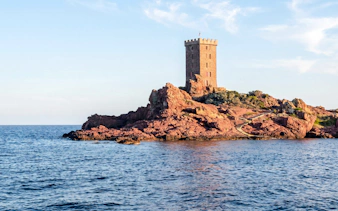 Catamaran cruise view of a coastal tower on red rocks at sunset.