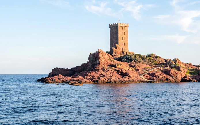 Catamaran cruise view of a coastal tower on red rocks at sunset.