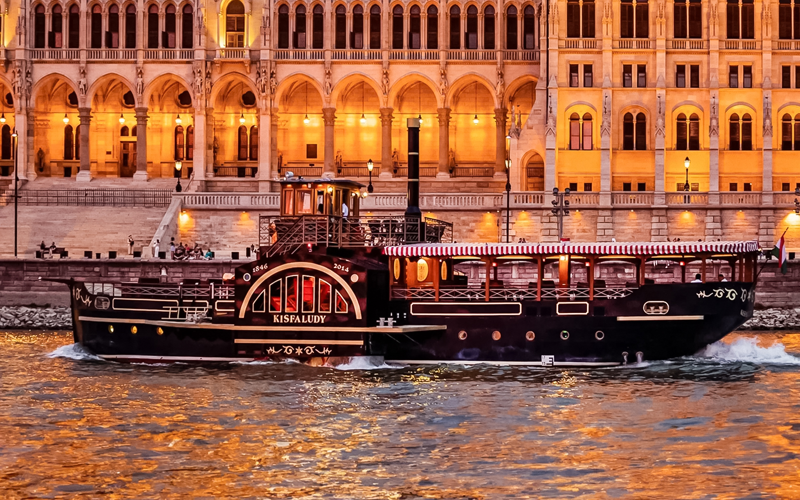 Historic cruise boat on the Danube River in Budapest with illuminated Parliament building backdrop.