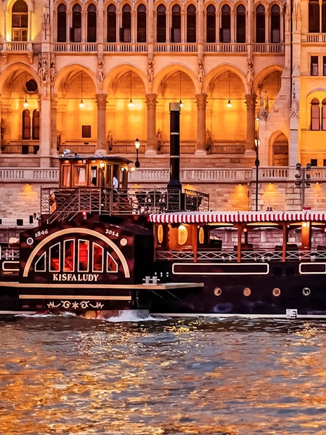 Historic cruise boat on the Danube River in Budapest with illuminated Parliament building backdrop.