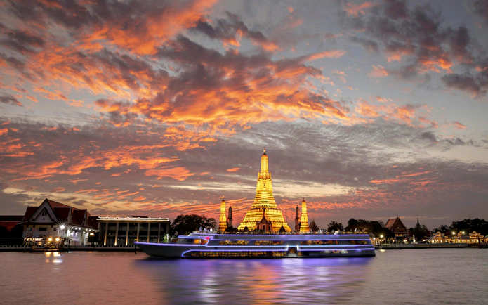 Chao Phraya River cruise boat with Wat Arun temple at sunset in Bangkok.