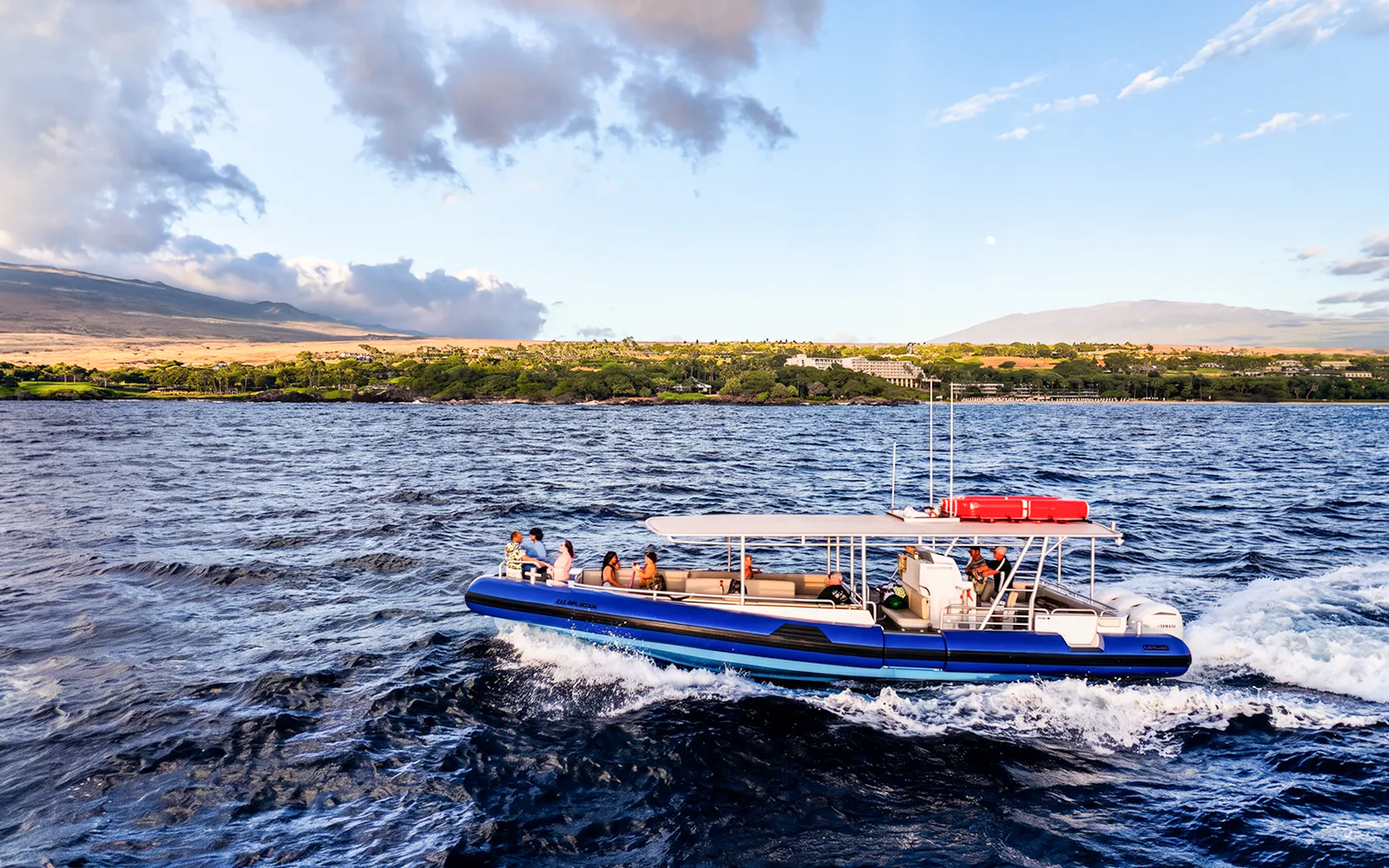 Boat cruising along Big Island’s Kohala Coast with scenic landscape in background.