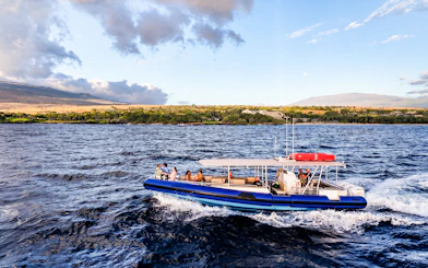 Boat cruising along Big Island’s Kohala Coast with scenic landscape in background.