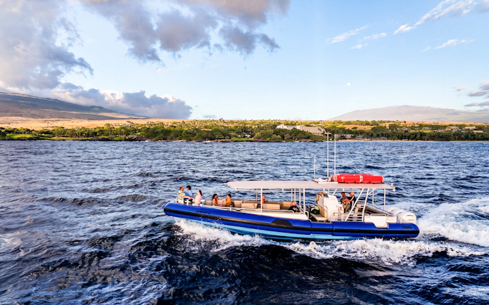 Boat cruising along Big Island’s Kohala Coast with scenic landscape in background.