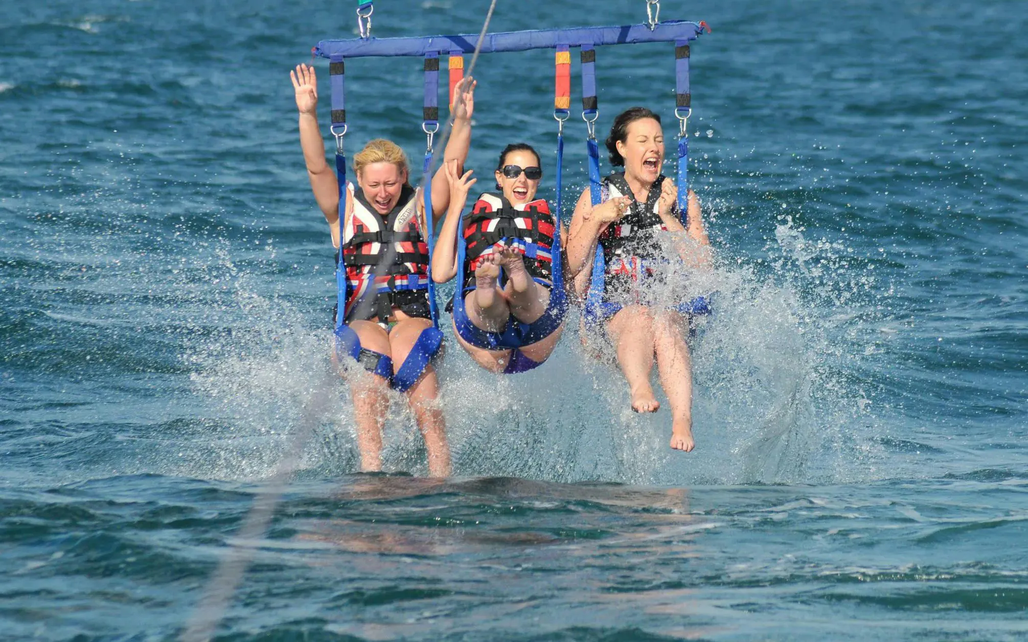Parasailing adventure over the ocean in Albufeira with three people splashing in the water.