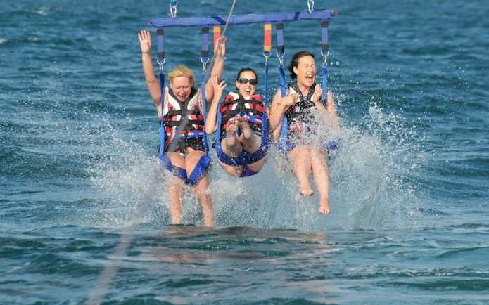 Parasailing adventure over the ocean in Albufeira with three people splashing in the water.