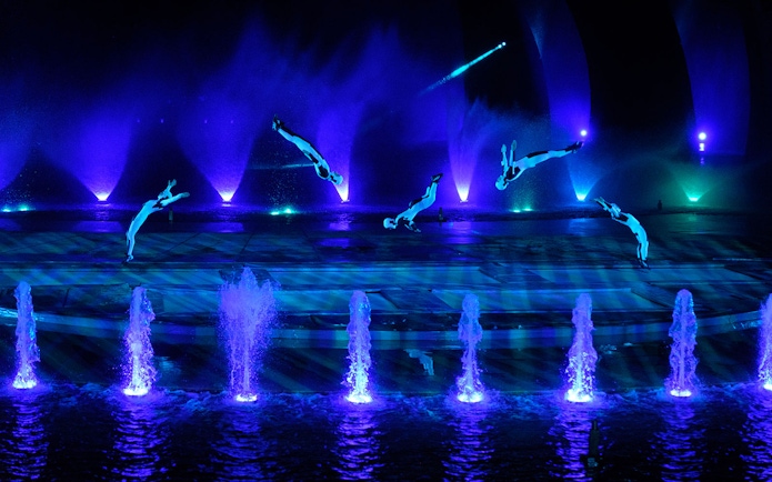 Acrobats performing mid-air flips over illuminated fountains at the Kiss of the Sea Show.