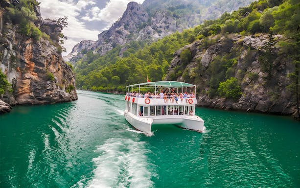 Tour boat navigating through rocky cliffs on Kekova Sunken City tour, Turkey.
