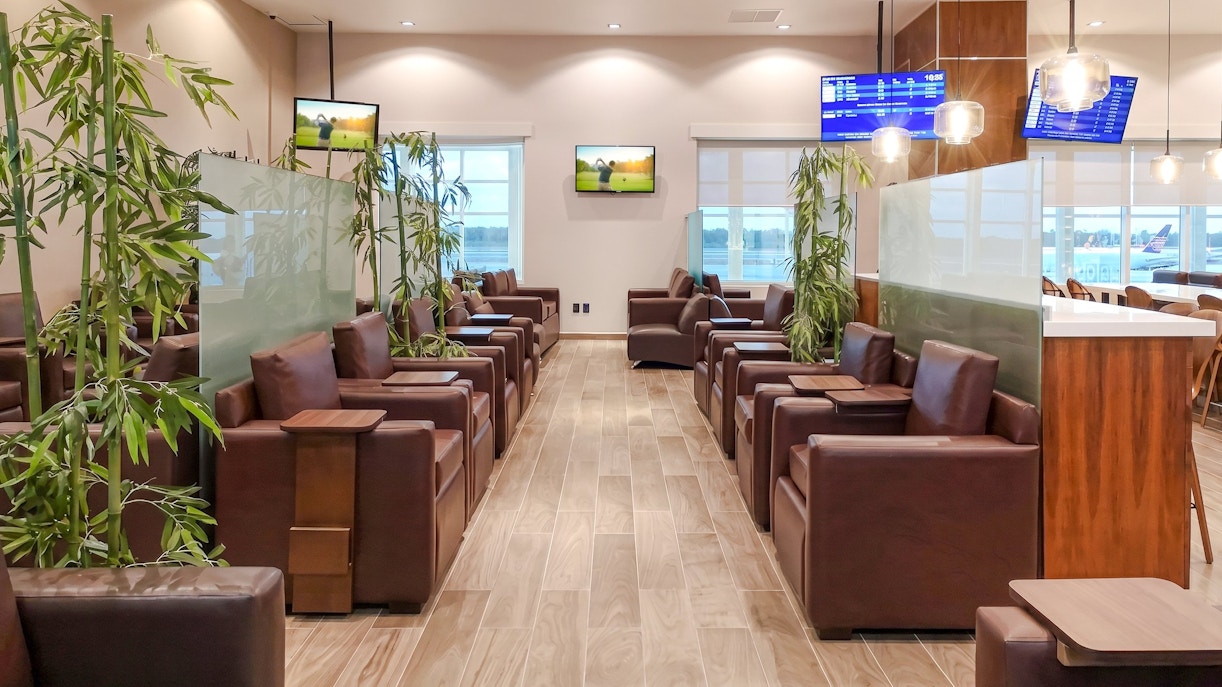 Lounge seating area with leather chairs and plants at MERA Business Lounge, Terminal 2, Cancún Airport.