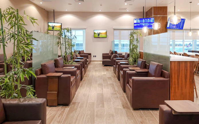 Lounge seating area with leather chairs and plants at MERA Business Lounge, Terminal 2, Cancún Airport.