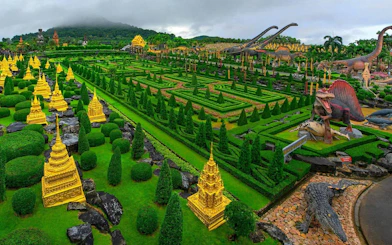 Nong Nooch Tropical Garden with dinosaur sculptures and golden pagodas in lush greenery, Thailand.