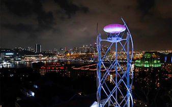 SkyHelix Sentosa ride illuminated at night with Singapore cityscape in the background.
