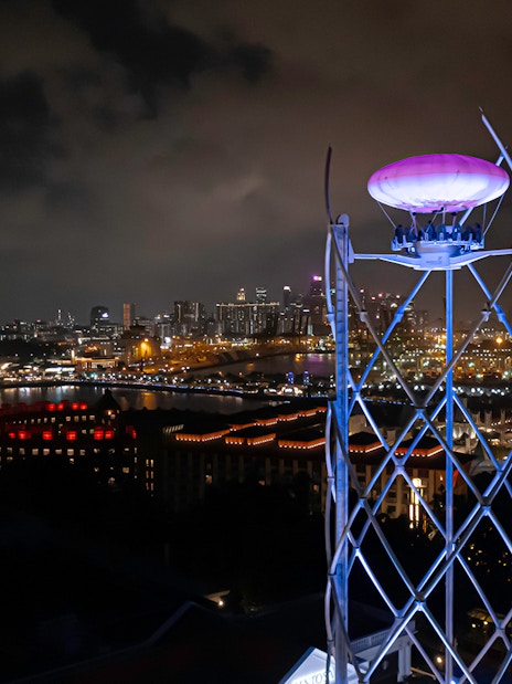 SkyHelix Sentosa ride illuminated at night with Singapore cityscape in the background.