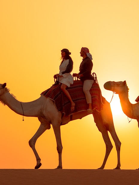 Tourists on camels led by a guide in the Dubai desert at sunset.