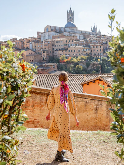 Person walking towards Siena Cathedral in Tuscany, Italy, surrounded by greenery.