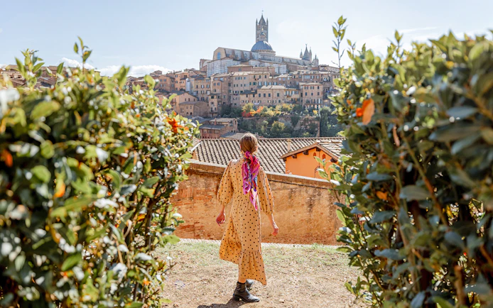 Person walking towards Siena Cathedral in Tuscany, Italy, surrounded by greenery.